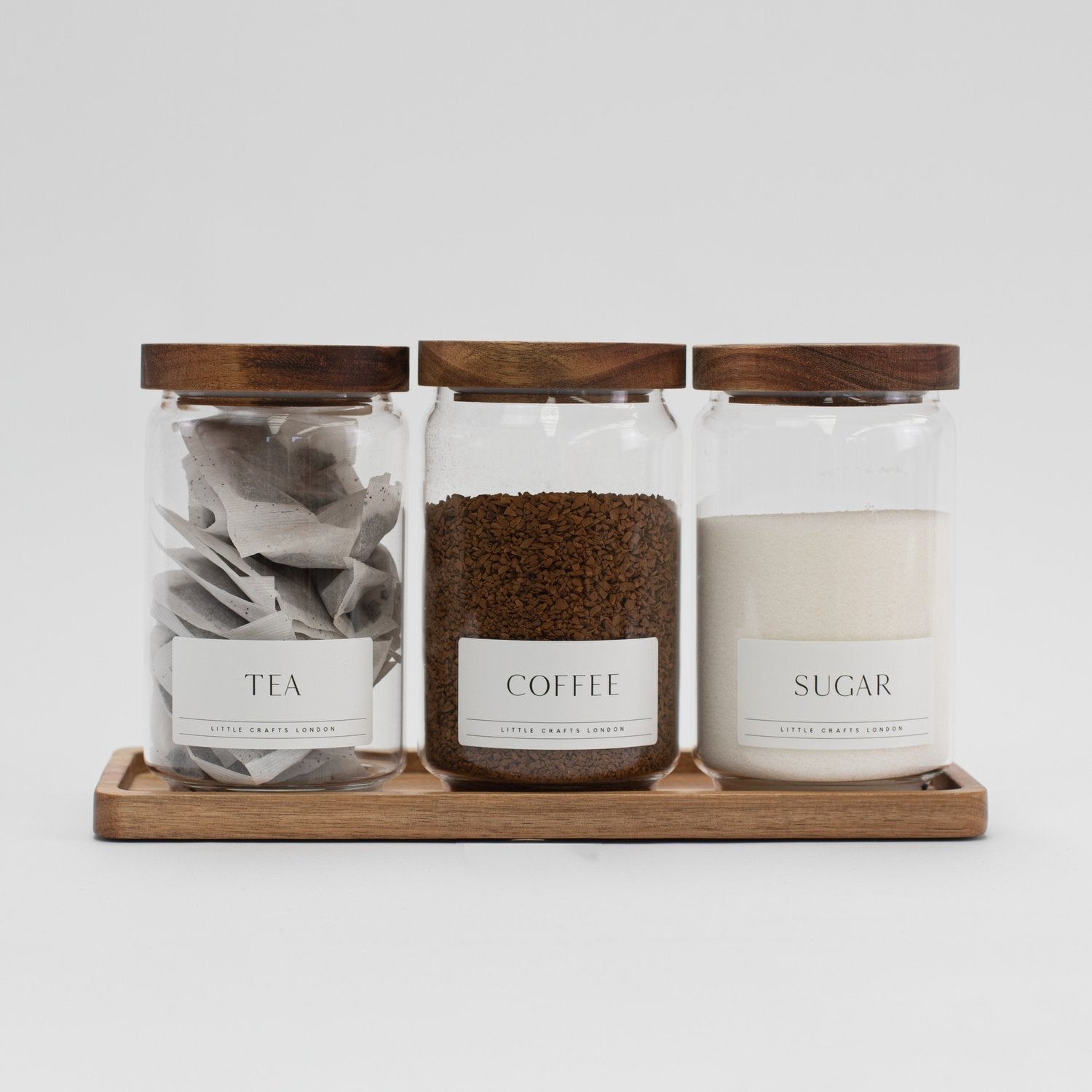 Main photo showing a stylish set of 3 glass jars with acacia wood lids, labelled Tea, Coffee & Sugar, on a matching rectangular tray – 750ml each.